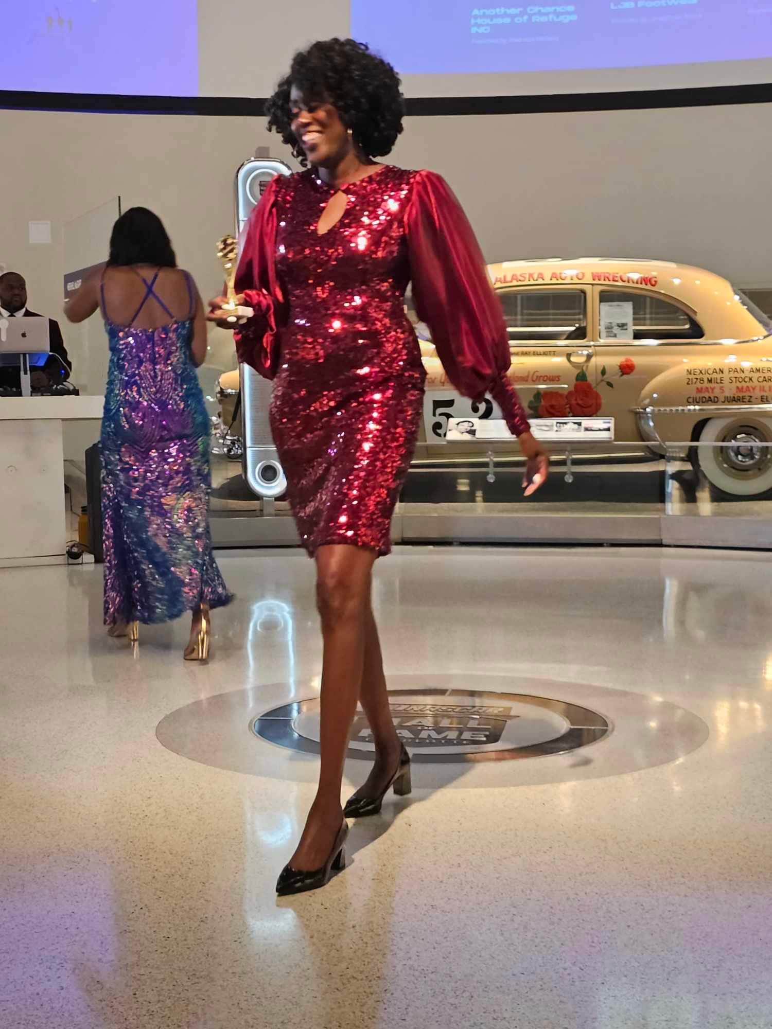 Honoree in red sequin dress walking with award